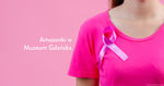 Zbliżenie na bark kobiety, ubranej w różową bluzkę z krótkimi rękawami. Do bluzki na piersi ma przypiętą różową wstążkę, symbol walki z rakiem piersi.