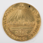 Zdjęcie, duże zbliżenie. Złota moneta. W centralnej części panorama miasta. Nad nią promienie, poniżej herb miasta. Wokół napis po łacinie.