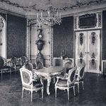 Zdjęcie czarno-białe. Wnętrze bogatego salonu. Pośrodku stół i sześć krzeseł. Nad nim kryształowy żyrandol. W tle dwuskrzydłowe drzwi, pod ścianą trzy fotele.