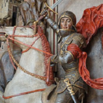 Zdjęcie rzeźby św. Jerzego z Dworu Artusa w Gdańsku. Rycerz w zbroi dosiada konia stojącego dęba. W prawej dłoni trzyma uniesiony miecz.