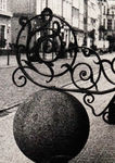 Zdjęcie czarno białe. Bogato zdobione zakończenie metalowej poręczy. Osadzone na kamiennej kuli, typowej dla gdańskich przedproży.