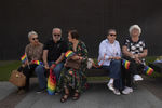 Zdjęcie. Na ławce siedzi pięć osób, cztery kobiety i mężczyzna. Wszyscy są w wieku senioralnym. W dłoniach trzymają tęczowe flagi, a mężczyzna tęczową torbę na zakupy. Siedzą na tle Teatru Szekspirowskiego.