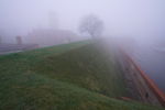 Fort z wieżą we mgle. Na pierwszym planie szaniec, za nim po prawej Wisła.