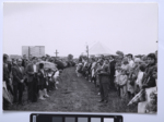Zdjęcie czarno-białe. Pierwsza msza na gdańskiej Zaspie. Tłum ludzi, pomiędzy nimi przejście. Patrzą w stronę fotografa. Za tłumem stoi krzyż. W tle bloki.