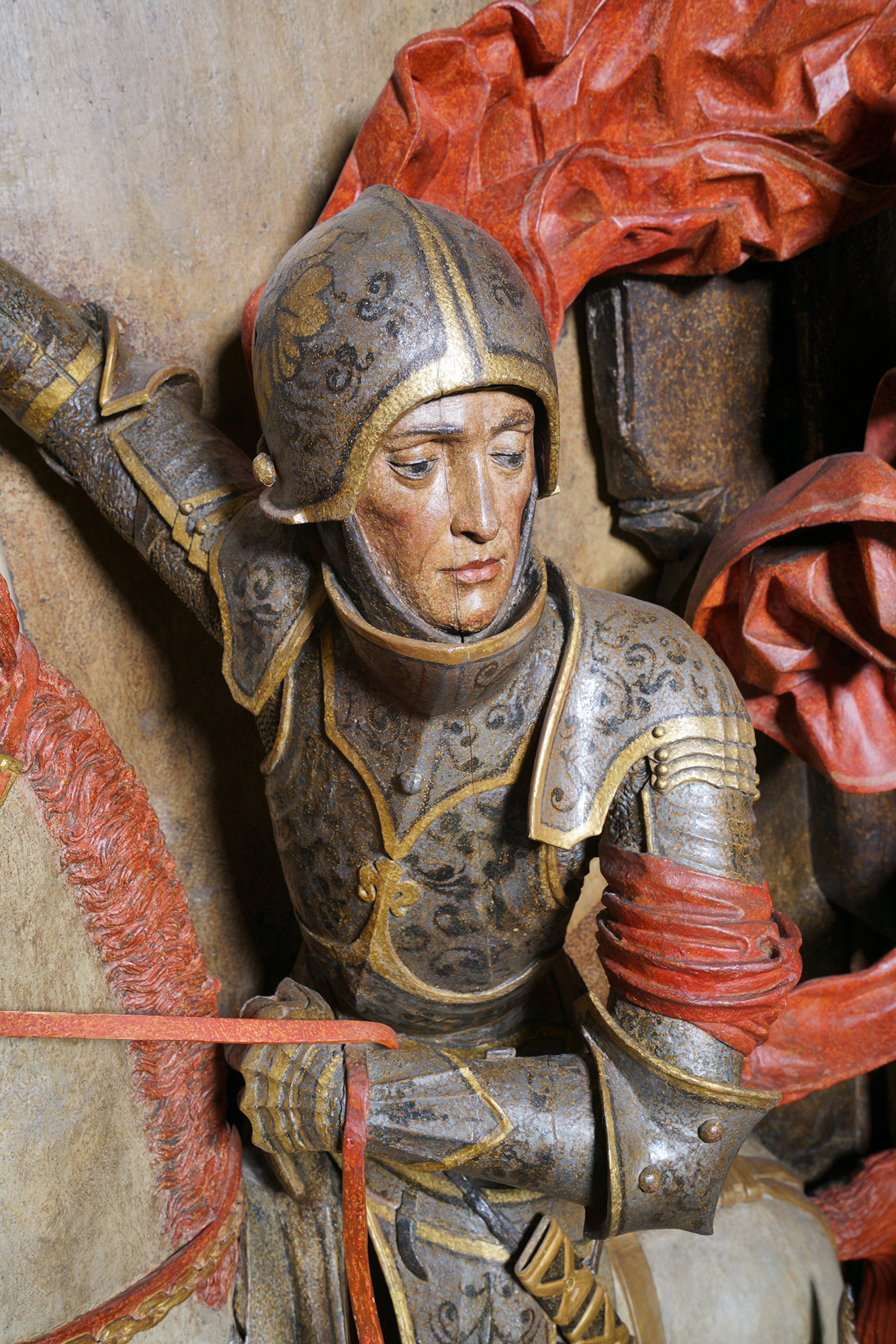 Fragment rzeźby św. Jerzy walczący ze smokiem. Rycerz w zbroi, widok do pasa. W lewej ręce trzyma uzdę konia.