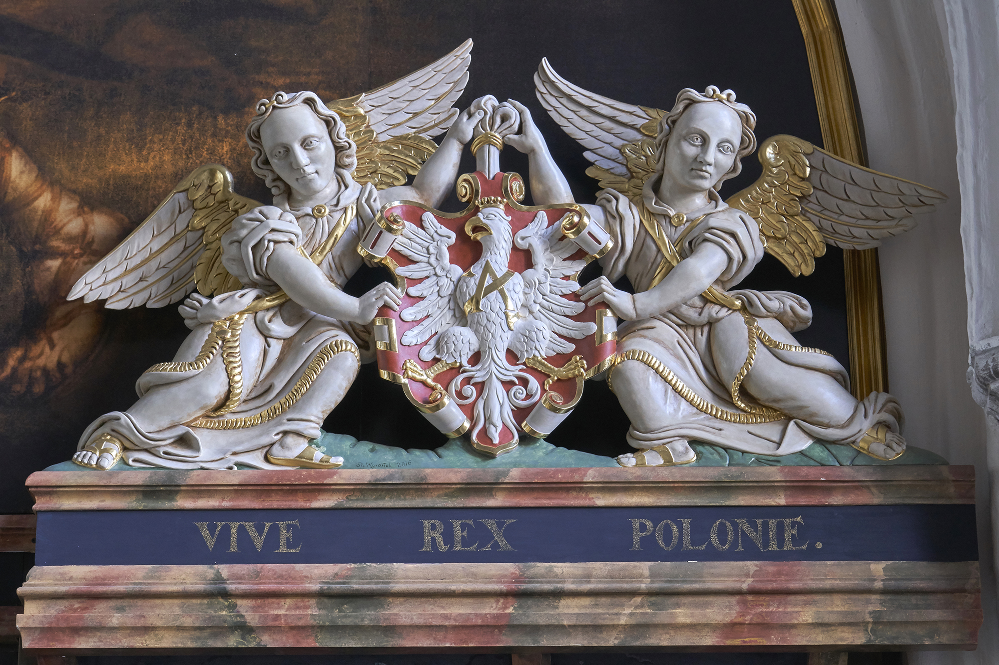 Dwa białe anioły, podtrzymują godło Polski. Poniżej napis Vive rex Polonie.