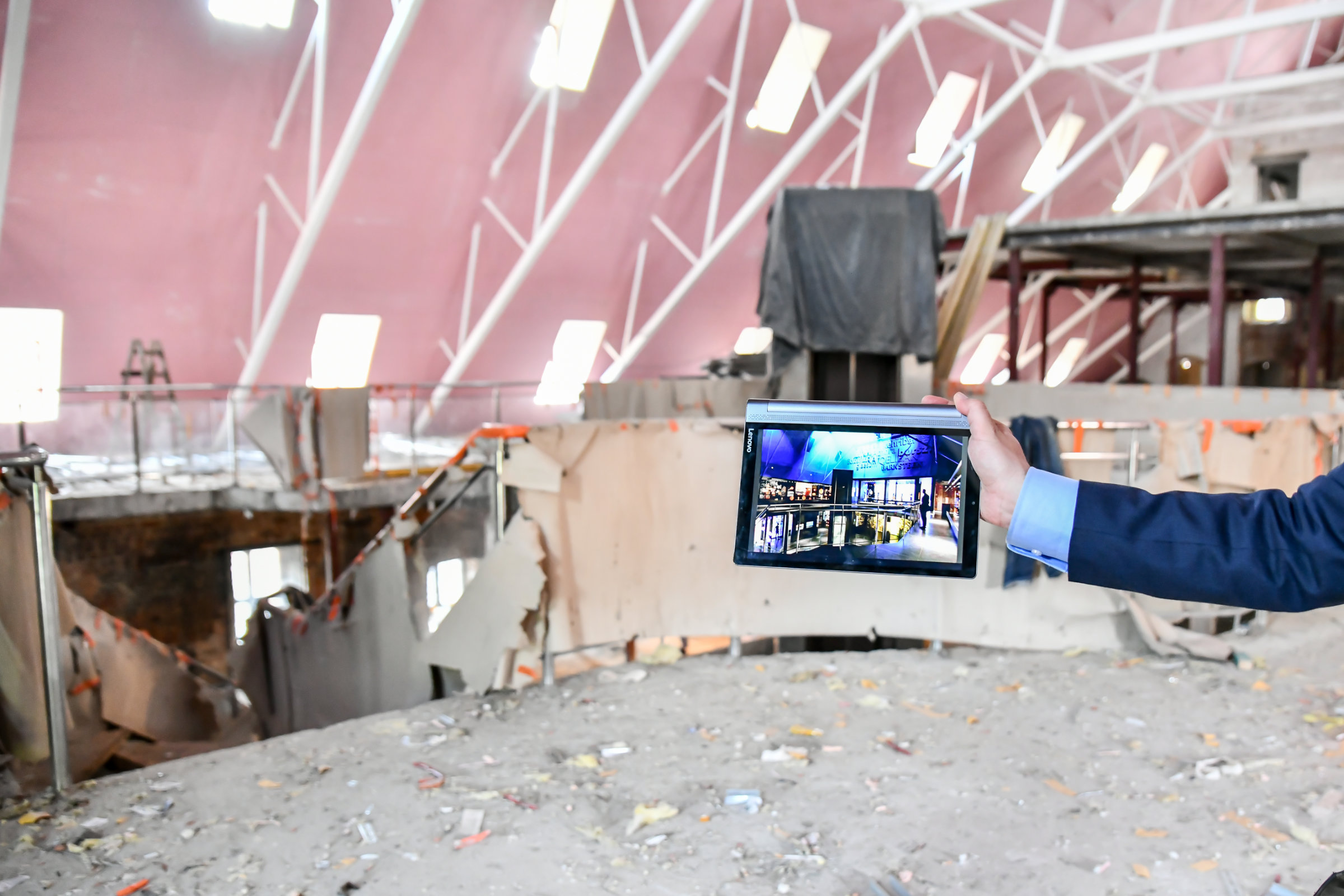 Zdjęcie z budowy nowego Muzeum Bursztynu. Na pierwszym planie wyciągnięta ręka, trzyma tablet. Na ekranie wizualizacja nowego wnętrza.