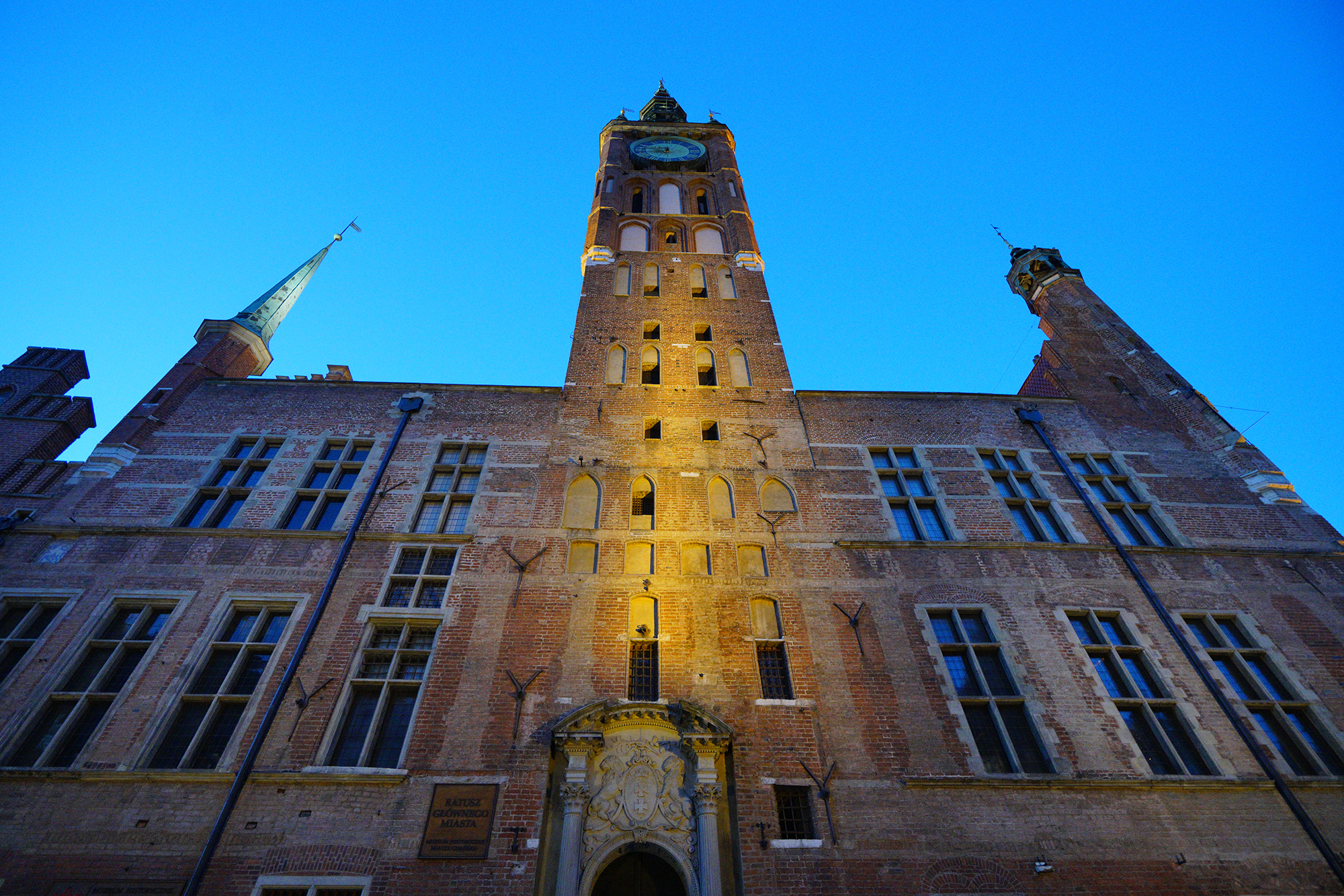 Widok na wieżę Ratusza z ulicy Długiej. W dole portal wejściowy zwieńczony herbem Gdańska. Na samej górze widać tarczę zegarową.