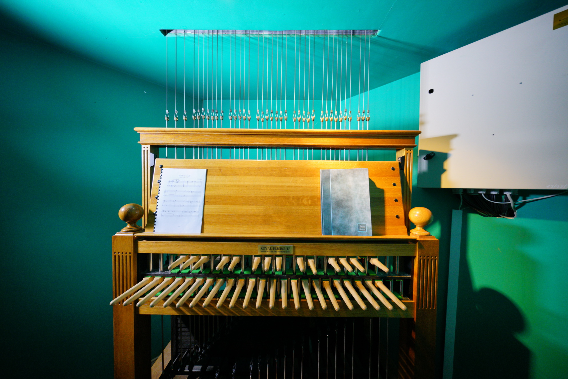 Pomieszczenie z konsolą carillonu. W suficie niewielki prostokątny otwór. Przechodzą przez niego liny łączące dzwony z klawiaturą.
