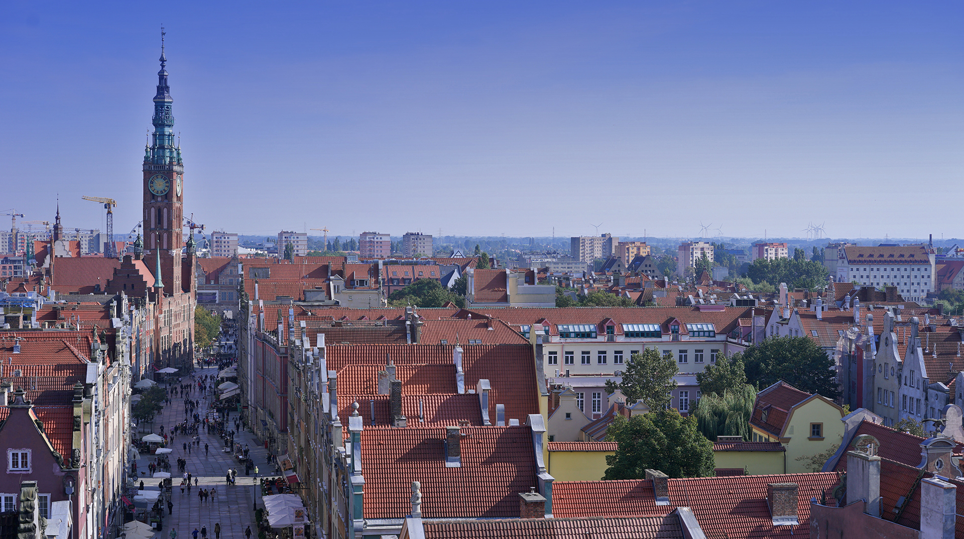 Panorama miasta, widok na kamieniczki przy ulicy Długiej. W głębi Ratusz Głównego Miasta. W oddali bloki mieszkalne, dachy budynków.