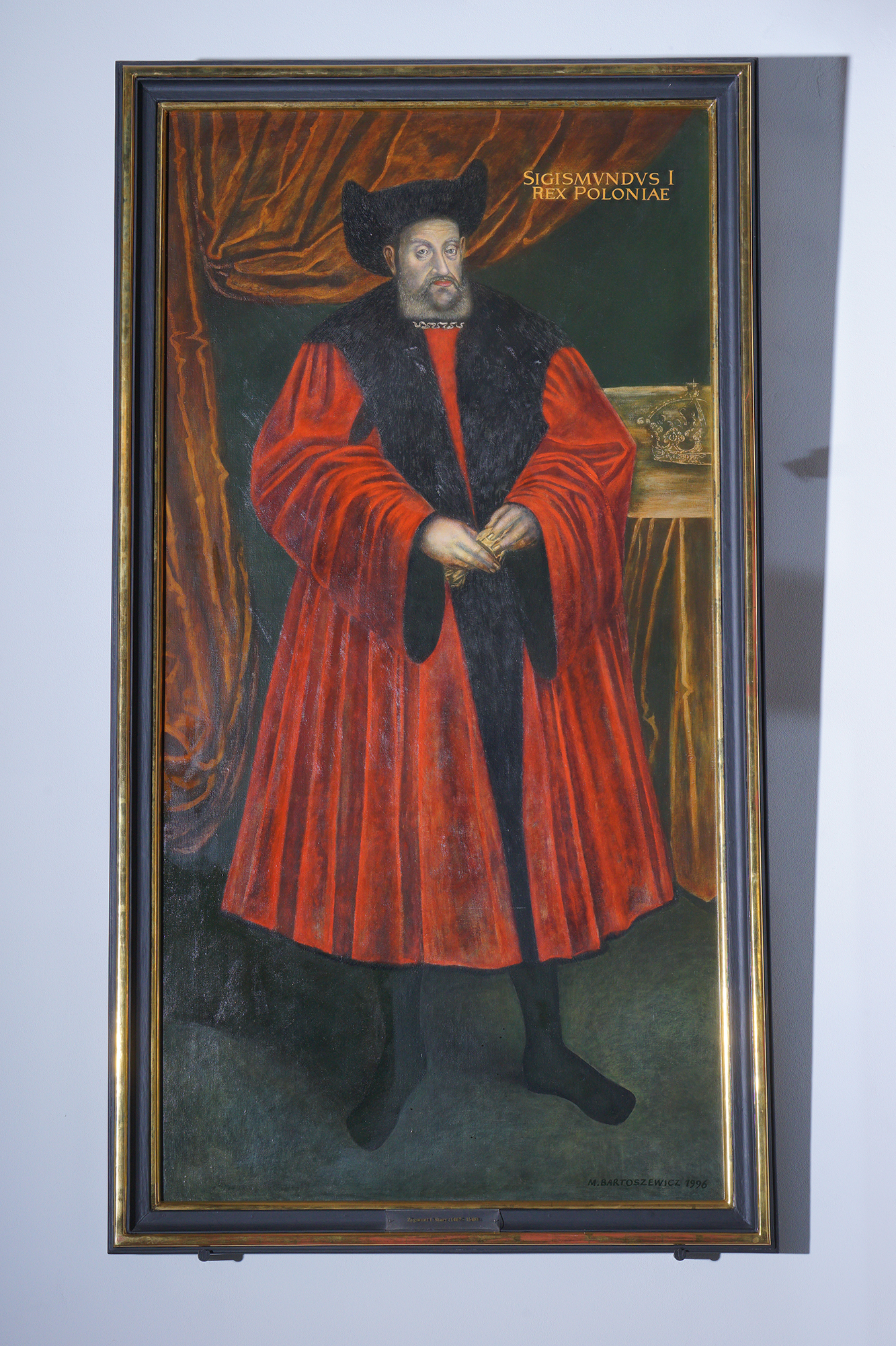 Portret króla Zygmunta I w Wielkiej Sali Wety. Ubrany w czerwone szaty. Na głowie ma czarny kapelusz.