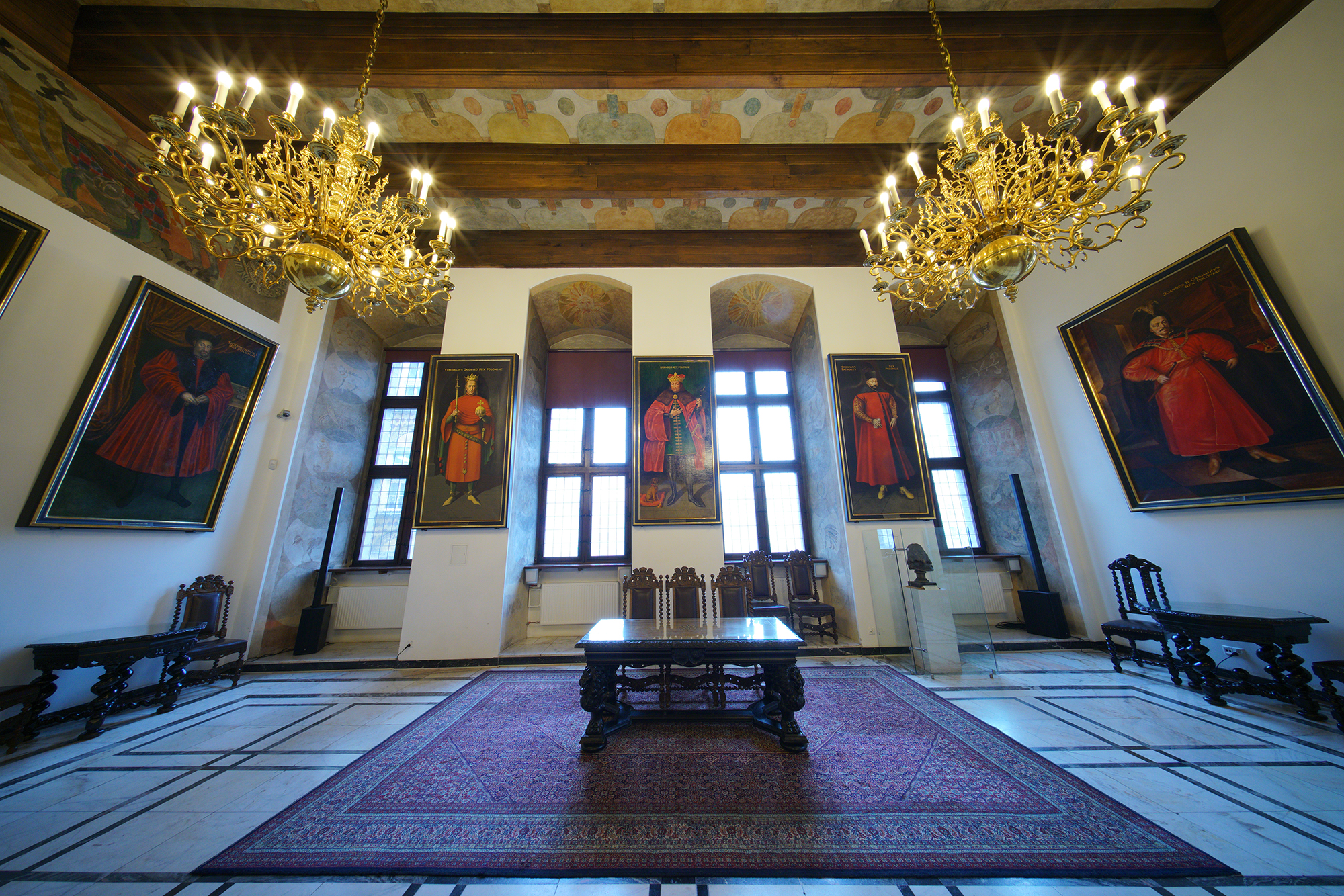 Wielka Sala Wety. Na ścianach wiszą obrazy królów Polski. Pośrodku, na dywanie stoją meble gdańskie - stół i trzy krzesła.