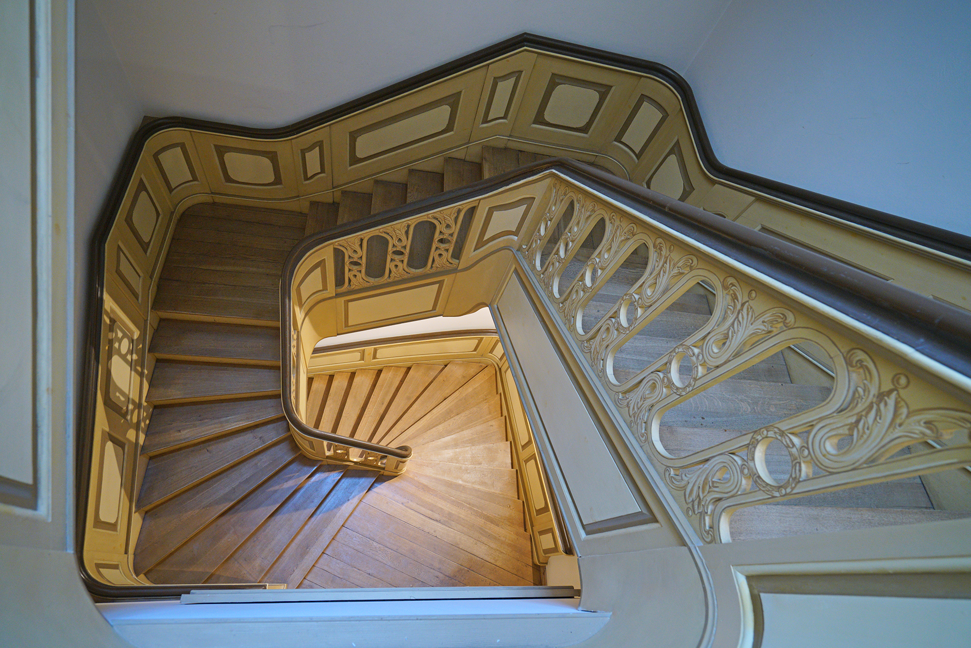 Zdjęcie klatki schodowej, zrobione ze szczytu schodów. Drewniane stopnie, rzeźbiona balustrada.
