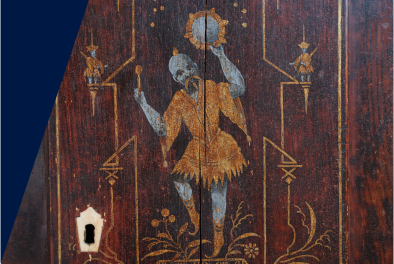 Zdjęcie malunku na drewnie. Postać męska trzyma w ręku tamburyn, tańczy. Ma na sobie złotą tunikę, duże wąsy, niebieski odcień skóry. W lewym dolnym rogu zdjęcia widać ślad po dziurce od klucza.